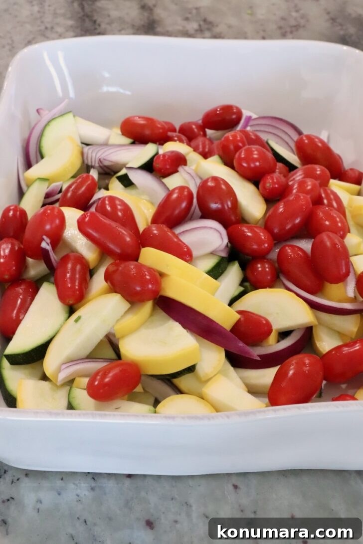 sliced yellow squash, zucchini, asparagus and onions in a large baking dish with cherry tomatoes