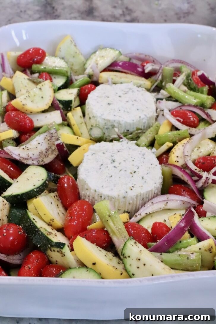 A white dish filled with vibrant chopped vegetables, including cherry tomatoes, zucchini, squash, and red onion, surrounds two seasoned cheese rounds.