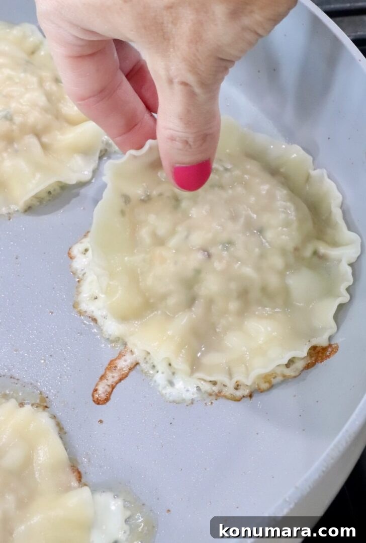 hand placing a ravioli on top of a mozzarella cheese crust in a skillet
