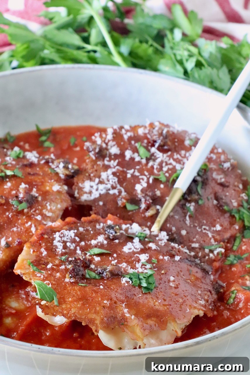 chicken ravioli with a mozzarella cheese crust in a bowl of marinara sauce with a fork, topped with fresh parsley and parmesan cheese