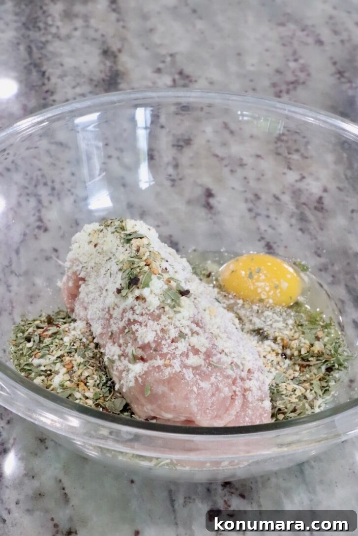 ground chicken in a glass bowl with parmesan cheese, breadcrumbs, an egg, and Italian seasoning