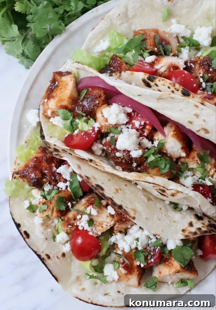 air fryer chicken tacos topped with diced tomatoes, pickled onions, cilantro, lettuce, and crumbled cheese on lightly charred tortillas.