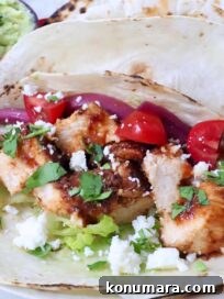 air fryer chicken tacos topped with diced tomatoes, pickled onions, cilantro, lettuce, and crumbled cheese on lightly charred tortillas.