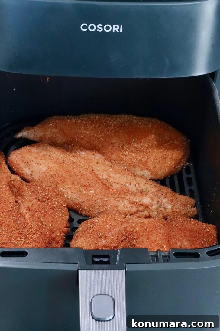 raw, seasoned chicken breasts in an air fryer basket