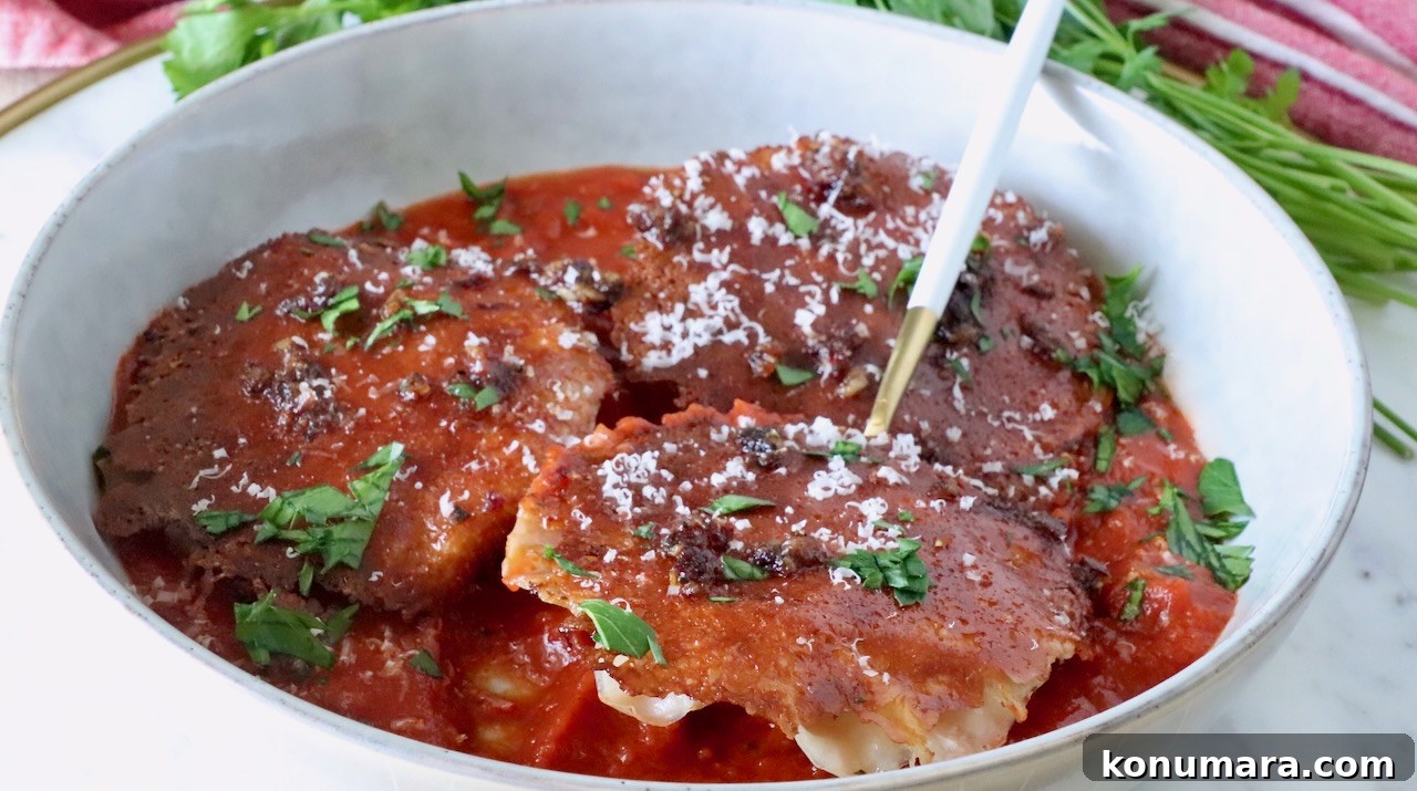 chicken ravioli with a mozzarella cheese crust in a bowl of marinara sauce with a fork, topped with fresh parsley and parmesan cheese