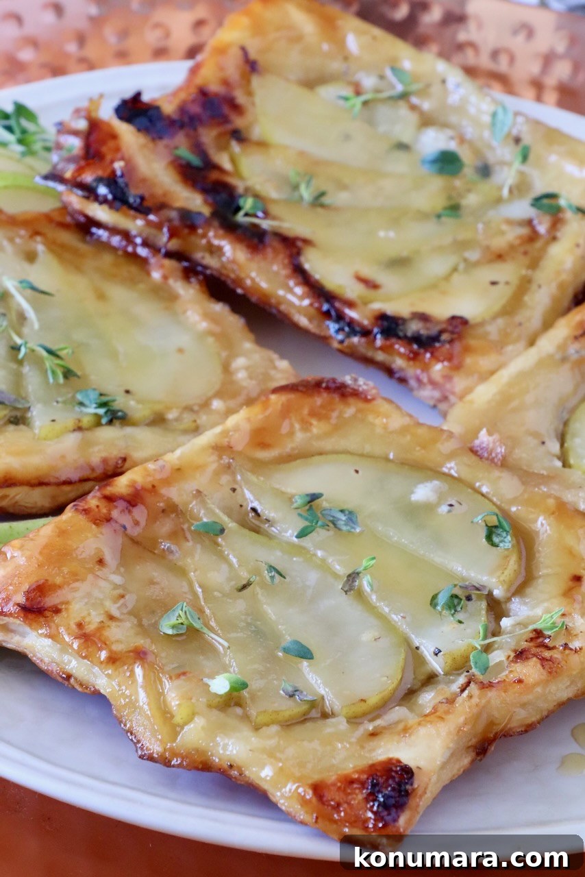 Close-up of golden-brown puff pastry tarts topped with sliced pears and drizzled with honey, garnished with fresh thyme leaves. 