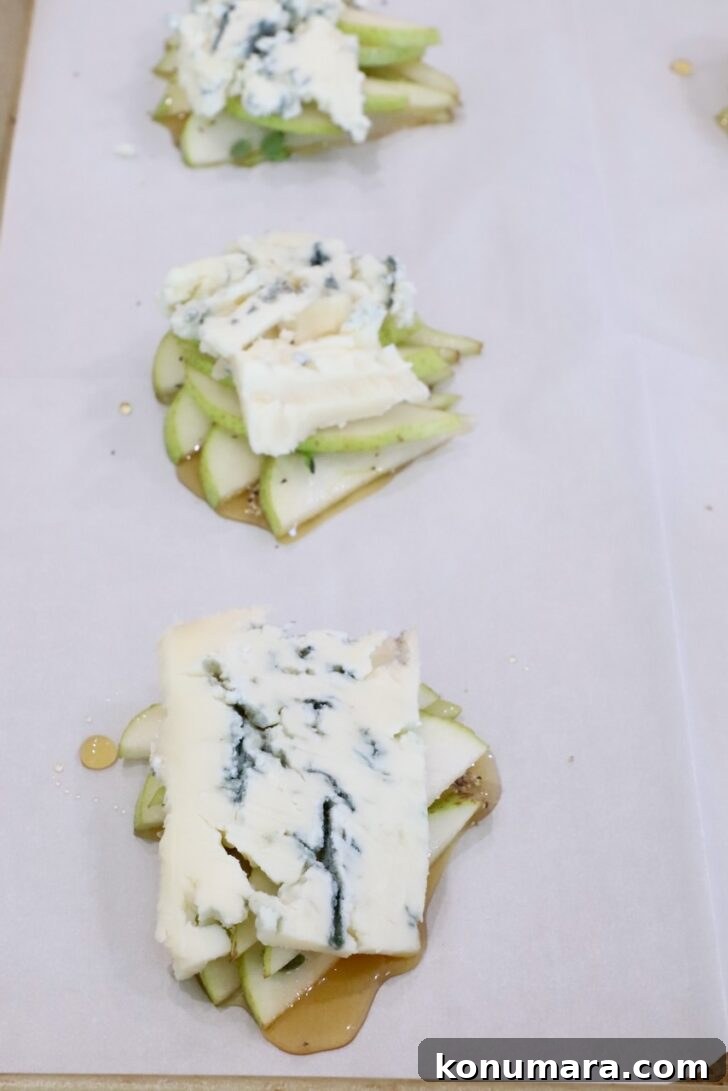 slices of gorgonzola cheese on top of sliced pears and honey on a sheet of parchment paper on a baking sheet