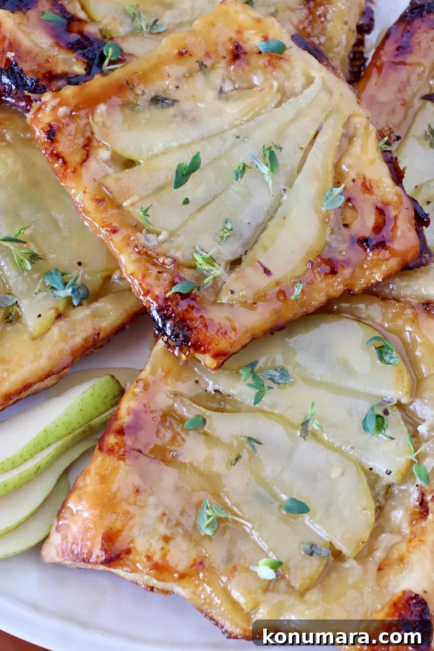 Golden brown pear tarts topped with fresh thyme, placed on a white plate.