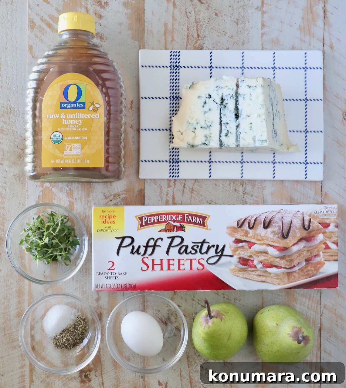 Ingredients on a wooden table include honey, gorgonzola cheese, fresh thyme leaves, salt, pepper, an egg, pears, and puff pastry sheets.