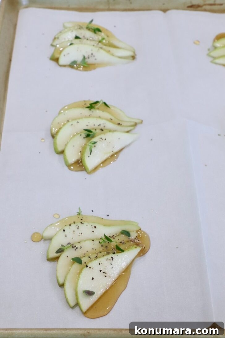 sliced pears topped with honey, salt, pepper, and fresh thyme, on a sheet of parchment paper on a baking sheet 