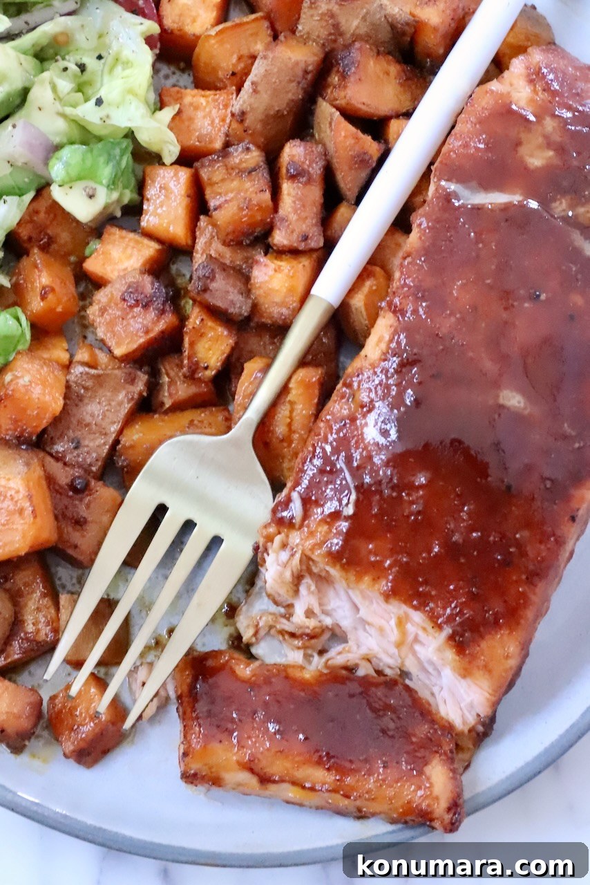 BBQ Salmon with Maple Glazed Sweet Potatoes 2 A plate of glazed salmon fillet, accompanied by seasoned sweet potato cubes and a side salad. A gold fork rests on the plate.
