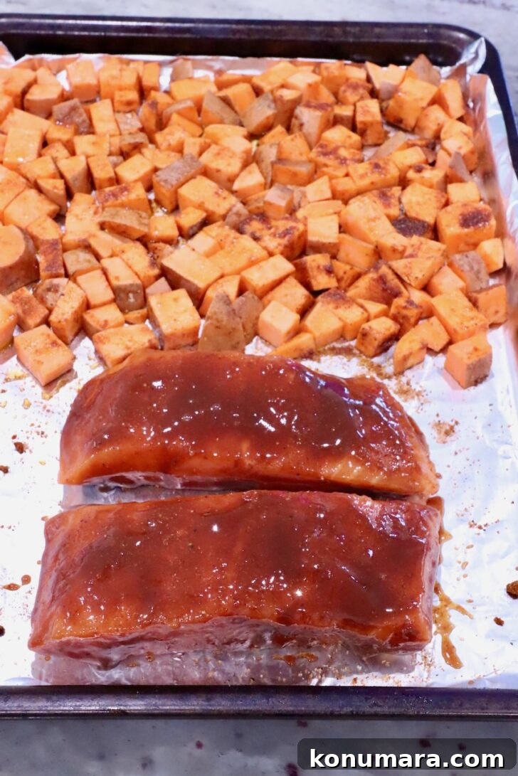 BBQ Salmon with Maple Glazed Sweet Potatoes 7 diced seasoned sweet potatoes on a foil lined baking sheet with two salmon filets coated in bbq sauce