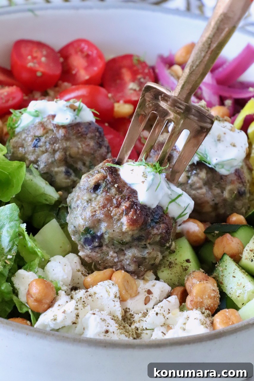 Gyro-Style Meatballs with Tzatziki Sauce 2 A bowl of vibrant Mediterranean salad with gyro meatballs topped with tzatziki sauce, sliced cherry tomatoes, cucumbers, crispy chickpeas, feta, and greens.