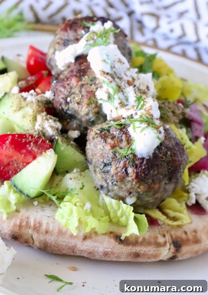 Gyro-Style Meatballs with Tzatziki Sauce 11 meatballs on top of pita bread on a plate, filled with lettuce, tomatoes, cucumber, and topped with creamy tzatziki sauce