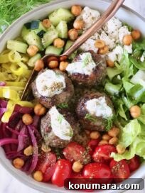 Gyro-Style Meatballs with Tzatziki Sauce 12 A colorful Mediterranean bowl with meatballs topped with yogurt sauce, surrounded by fresh lettuce, cherry tomatoes, cucumber, onions, and chickpeas.