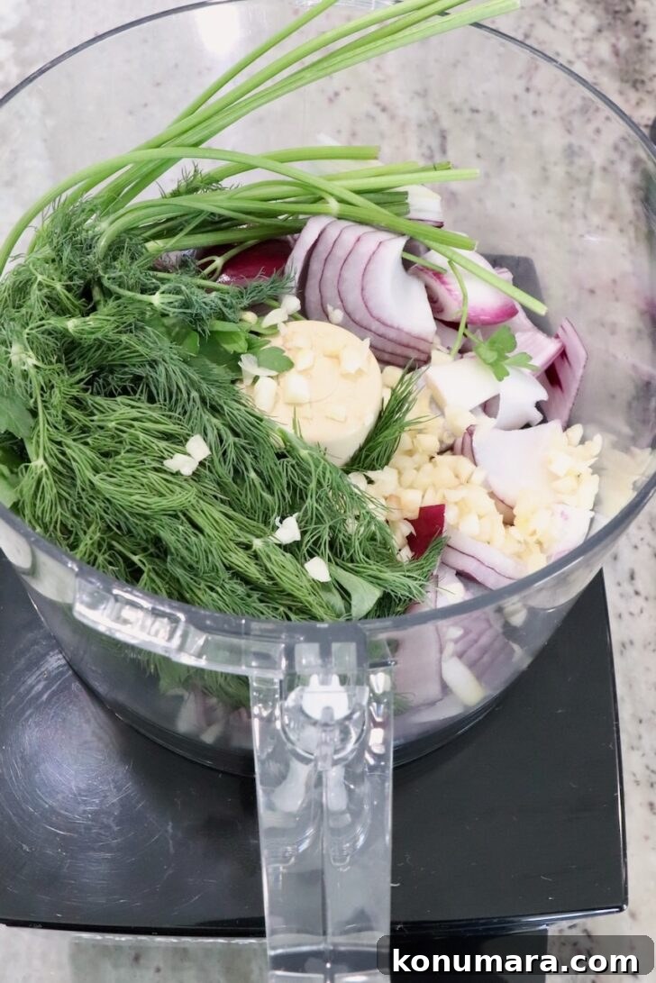 Gyro-Style Meatballs with Tzatziki Sauce 6 A food processor bowl filled with fresh herbs, sliced red onions, garlic, and parsley on a kitchen counter.