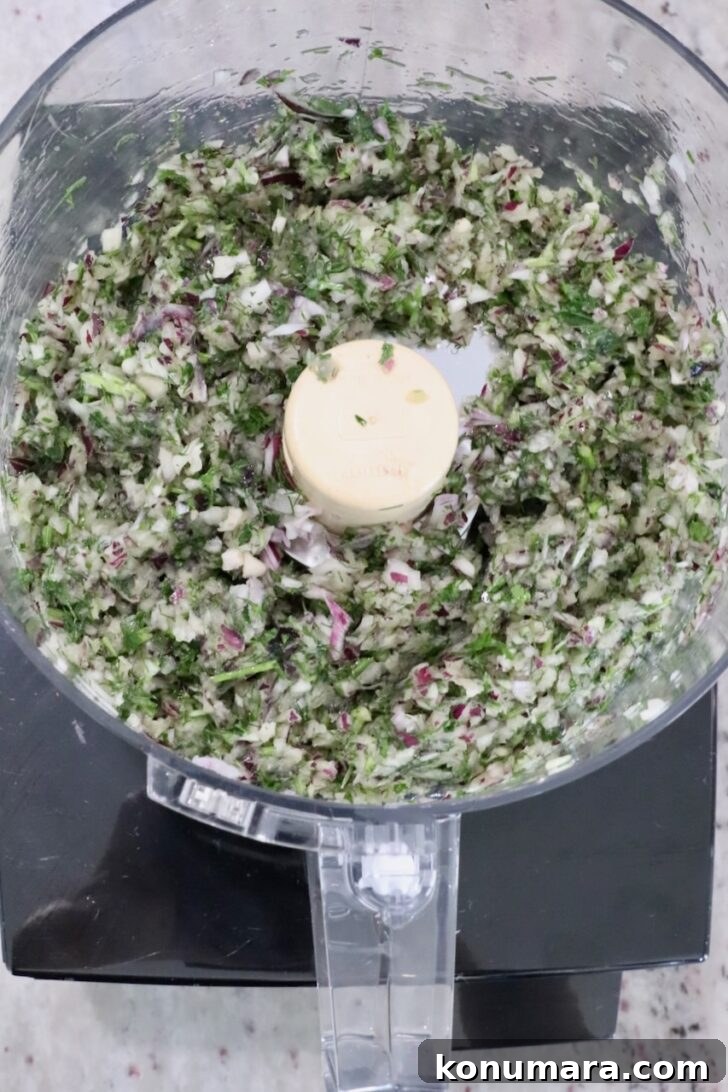 Gyro-Style Meatballs with Tzatziki Sauce 7 Chopped herbs and vegetables, including red onion and parsley, in a food processor bowl.