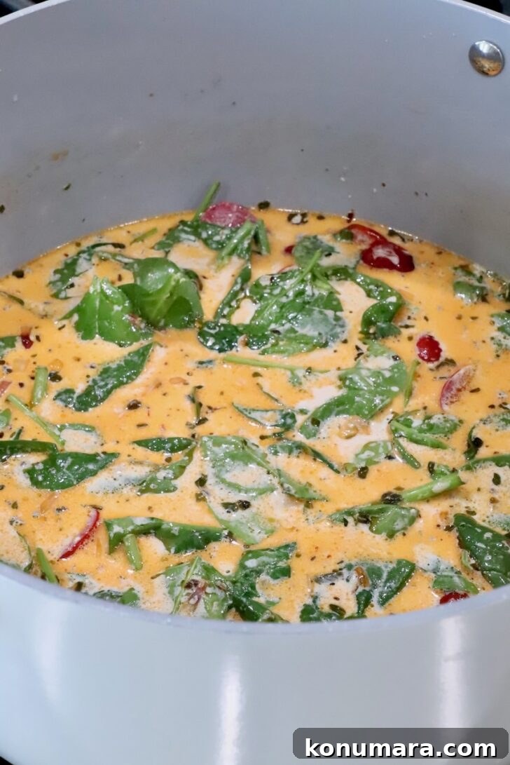 creamy tuscan sauce with spinach leaves and sun dried tomatoes in a sauce pan