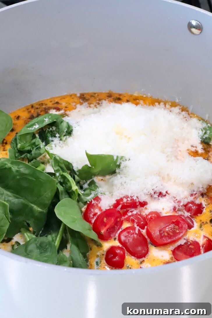 creamy sauce topped with diced cherry tomatoes, grated parmesan cheese and fresh spinach in a sauce pan