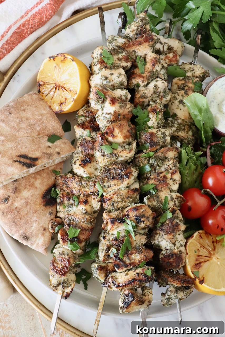 How to Make Authentic Greek Souvlaki 2 chicken souvlaki on skewers stacked up on a plate next to grilled pita bread, lemons and tomatoes