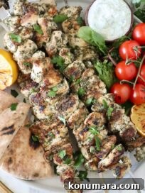 How to Make Authentic Greek Souvlaki 11 grilled chicken souvlaki on a plate with pita bread, a small bowl of tzatziki sauce, tomatoes, lemons, and herbs