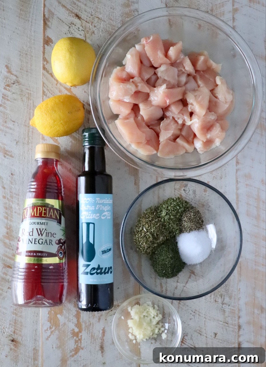 How to Make Authentic Greek Souvlaki 5 ingredients for souvlaki on a white wood board including a bowl of cubed chicken, olive oil, lemons, red wine vinegar, minced garlic, and spices