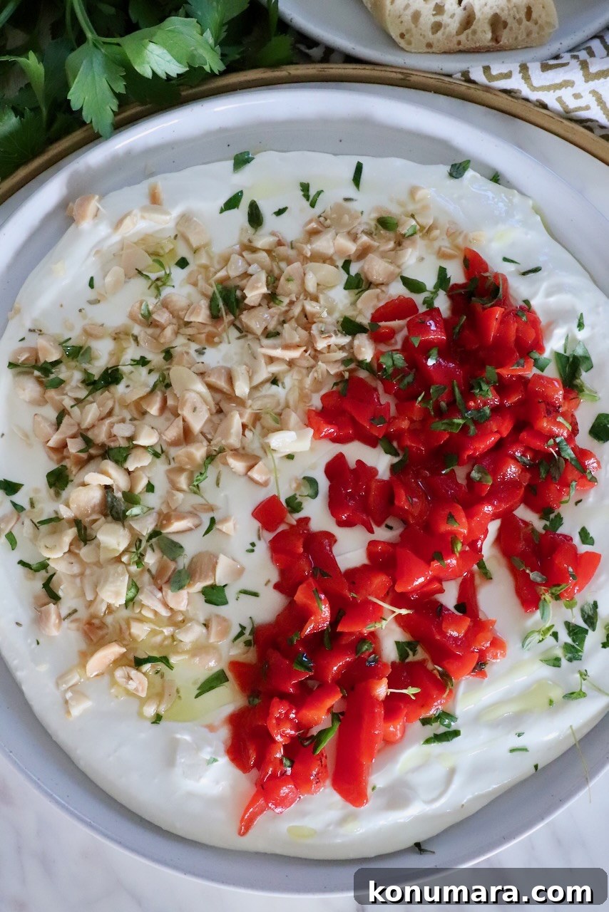 whipped goat cheese dip on a rimmed plate topped with chopped almonds, roasted red peppers and fresh herbs