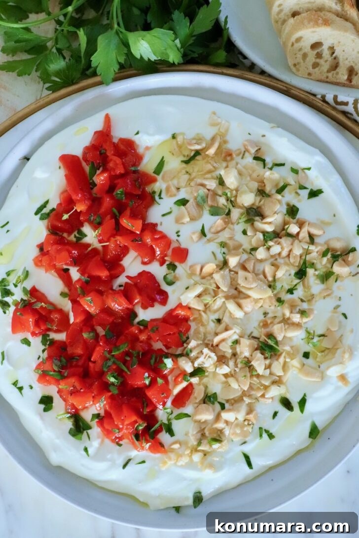 whipped goat cheese dip on a rimmed plate topped with chopped almonds, roasted red peppers and fresh herbs