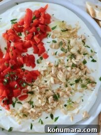 creamy goat cheese dip on a plate topped with chopped almonds, roasted red peppers, and fresh parsley, with a sliced baguette on the side