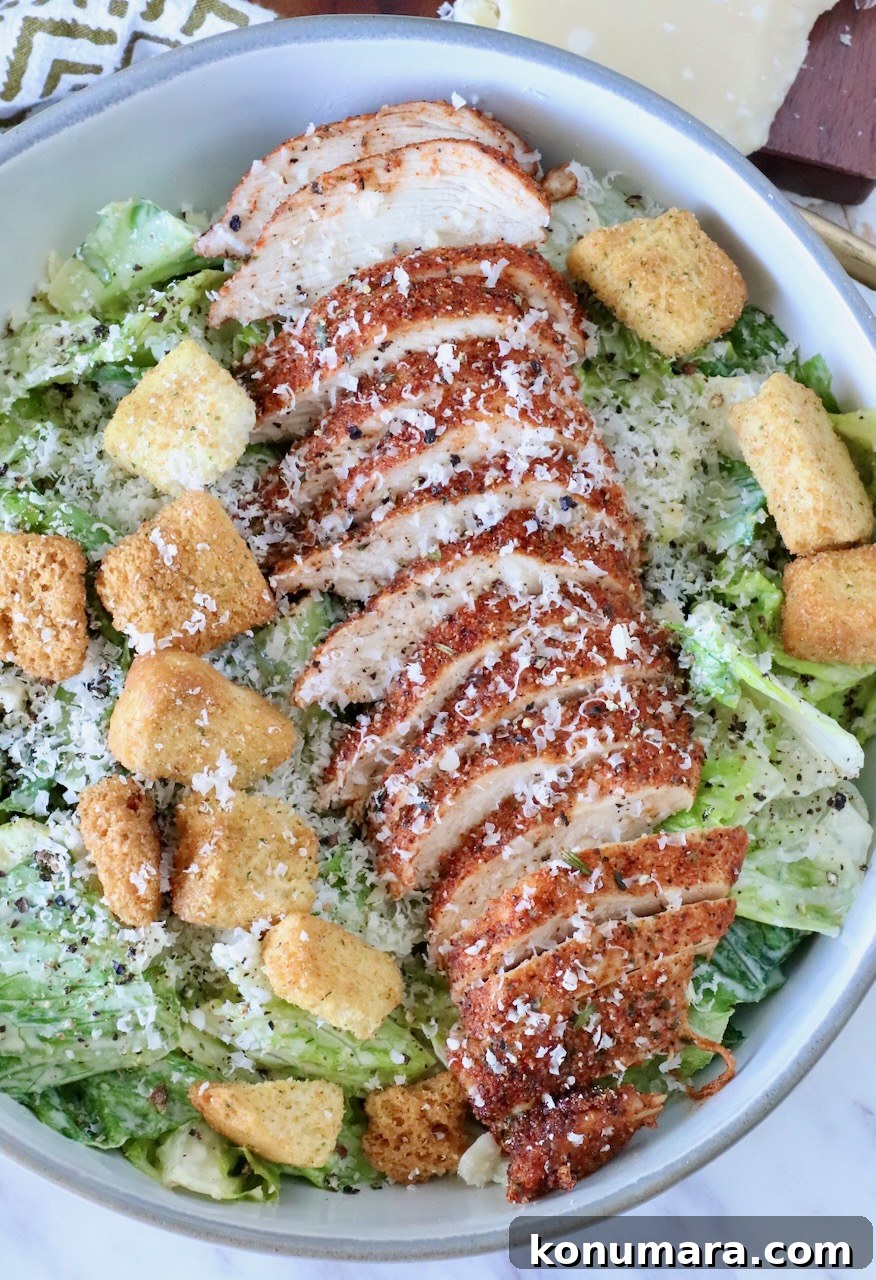 blackened chicken sliced on top of a caesar salad in a bowl with croutons