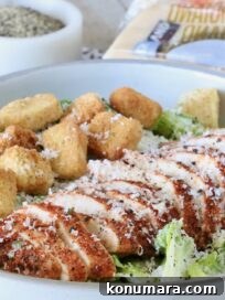 sliced blackened chicken on top of a salad in a bowl with croutons and grated parmesan cheese
