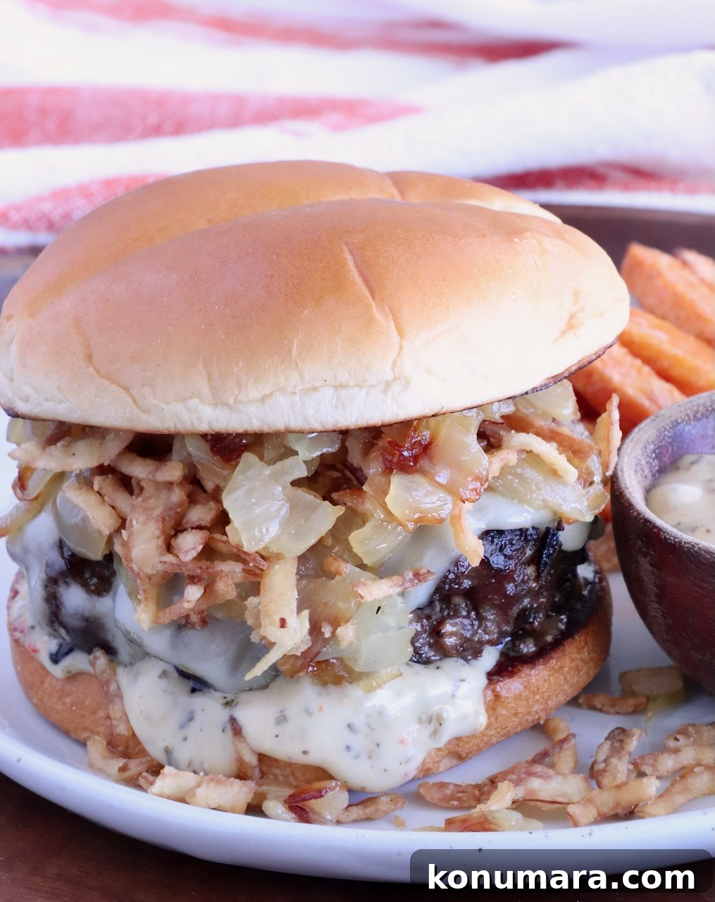 cheeseburger on a plate topped with caramelized onions and crispy fried onions, with a small bowl of sauce on the side