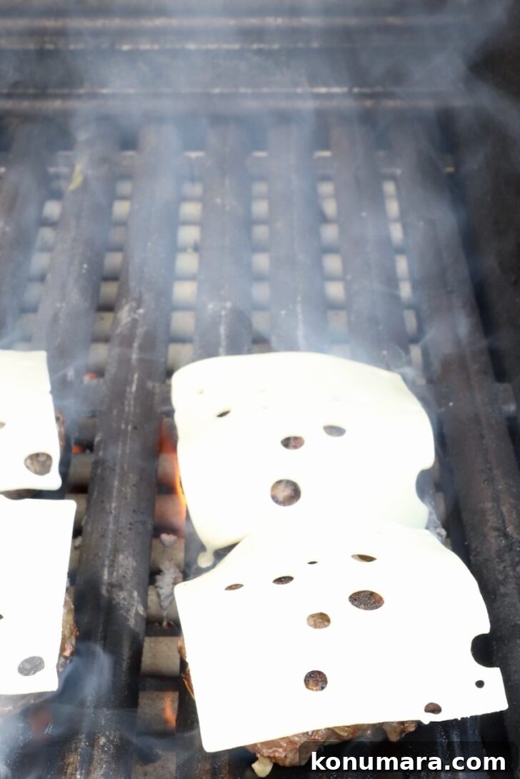 burger patties on a grill topped with sliced swiss cheese