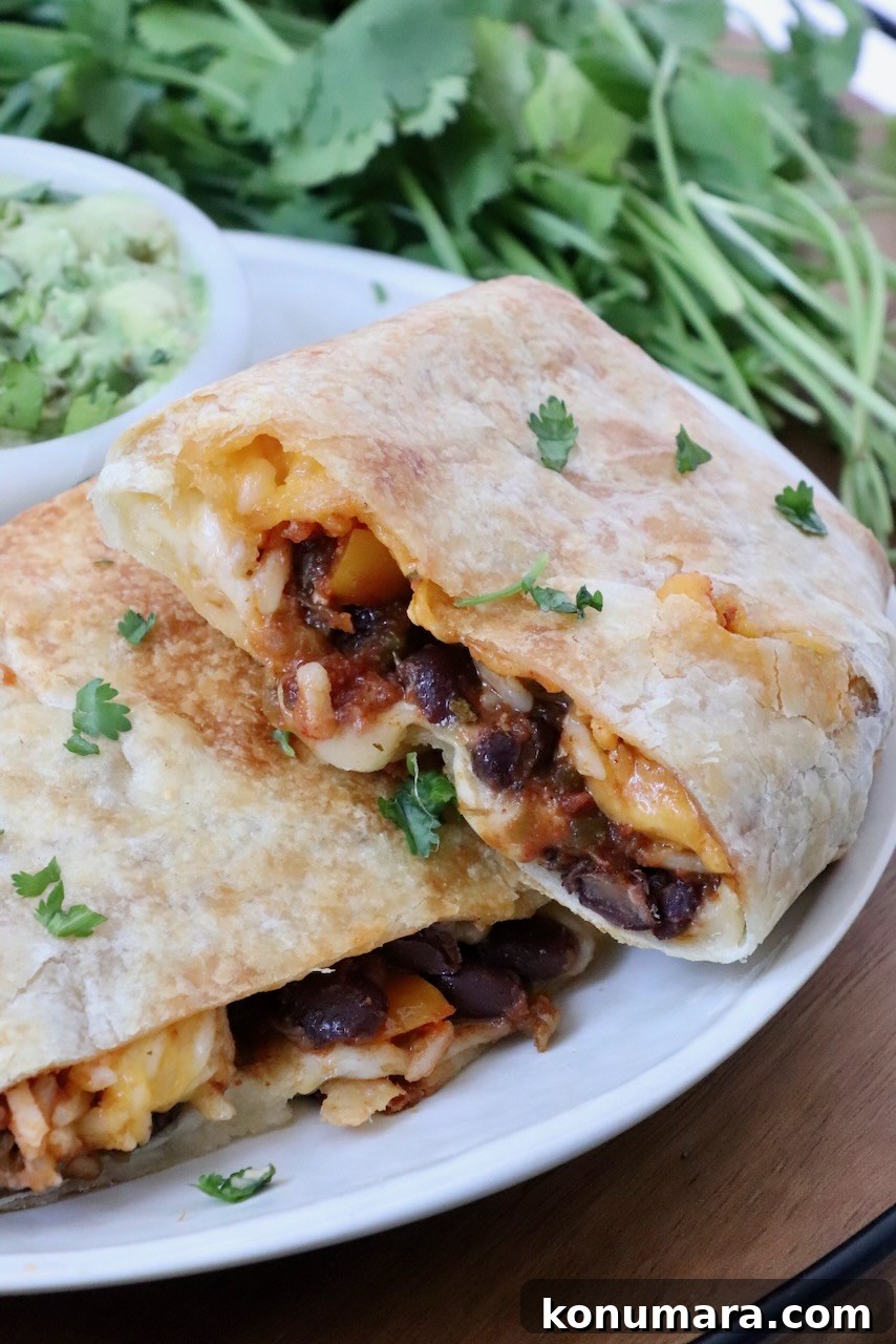 Vegetarian Cheesy Bean and Rice Burrito Recipe 2 bean and cheese burrito cut in half and stacked up on a plate with a bowl of guacamole and fresh cilantro in the background