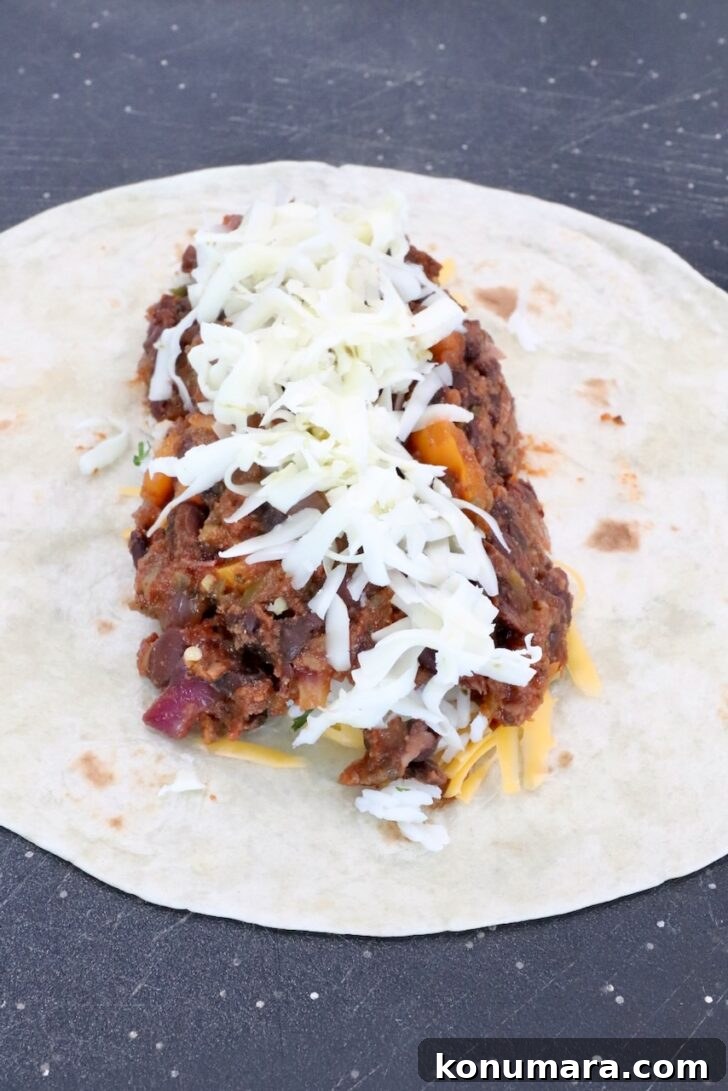 Vegetarian Cheesy Bean and Rice Burrito Recipe 11 bean filling in the middle of a tortilla topped with shredded pepper jack cheese