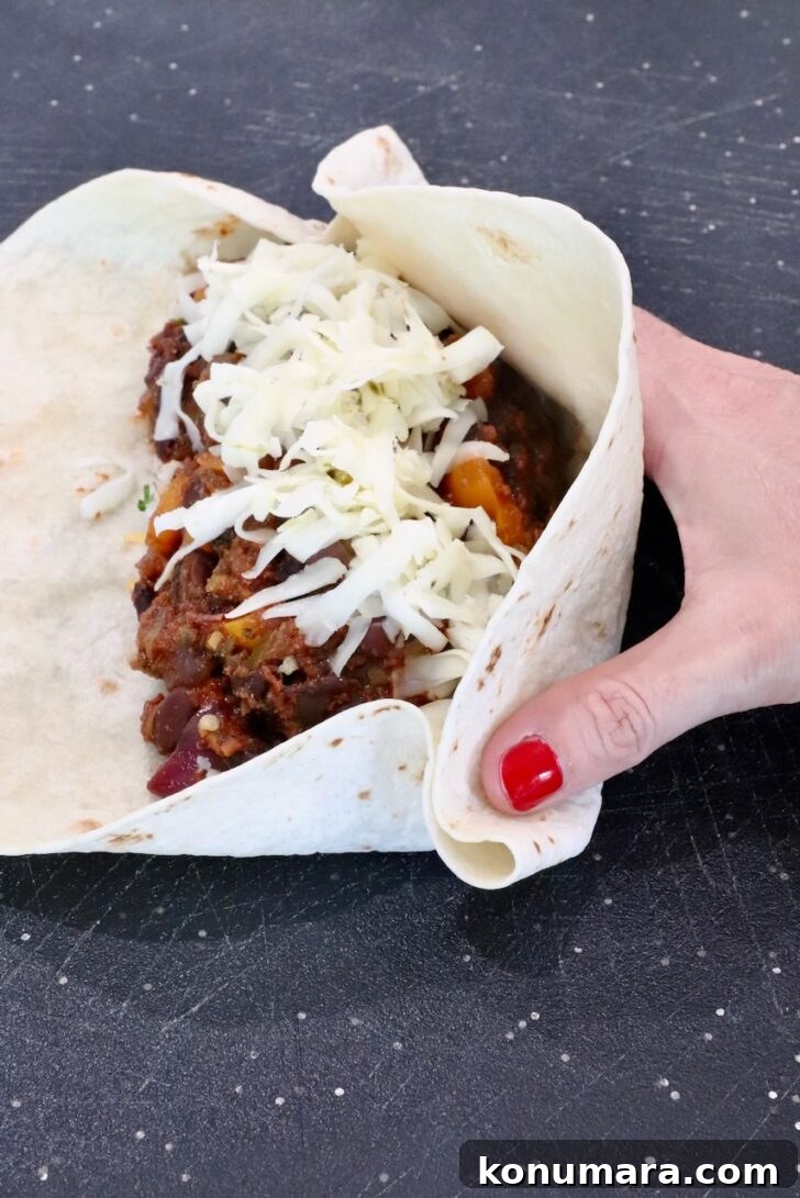 Vegetarian Cheesy Bean and Rice Burrito Recipe 12 hand folding a bean and cheese burrito on a cutting board