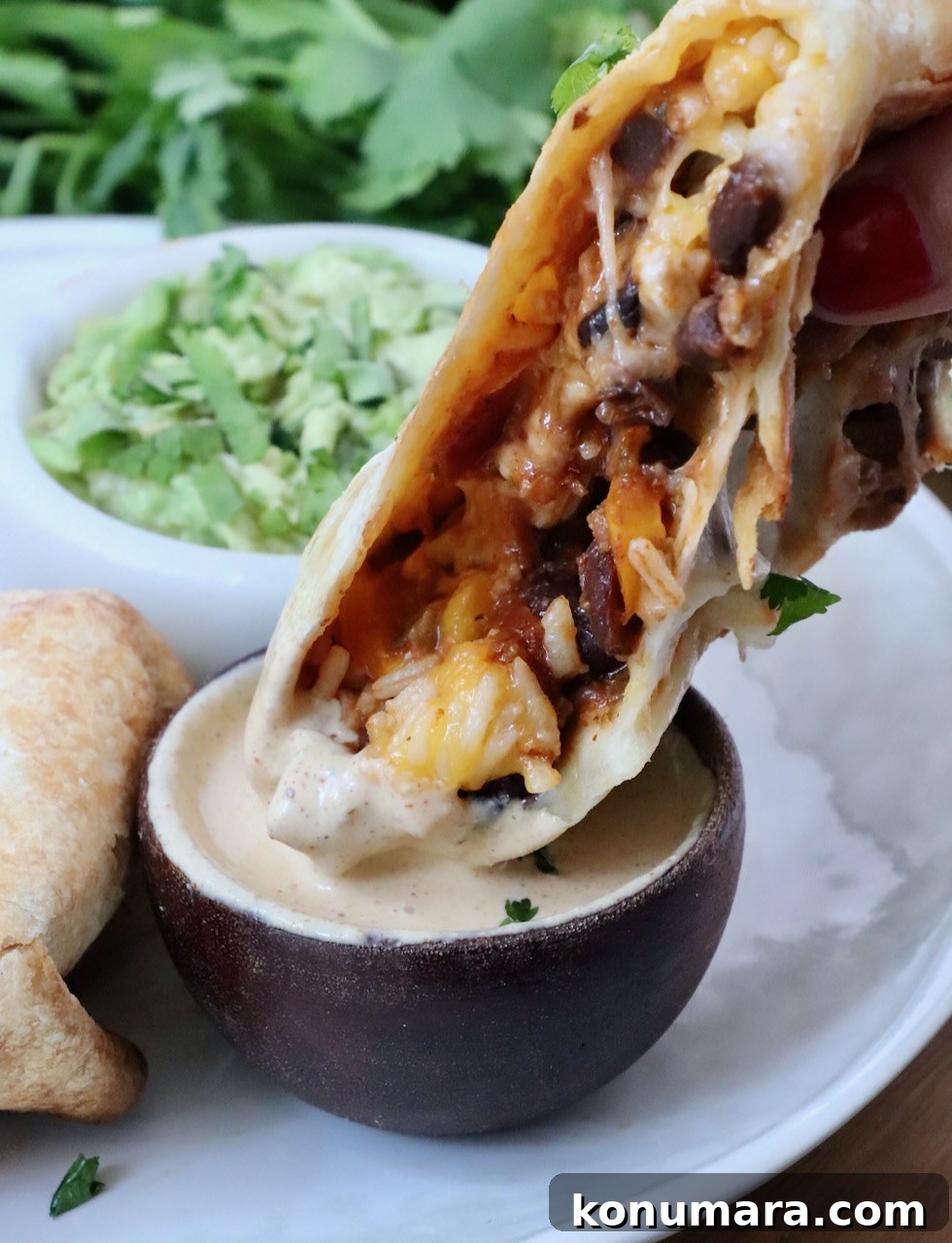 Vegetarian Cheesy Bean and Rice Burrito Recipe 15 half of a burrito dipped into a small bowl of sauce with a bowl of guacamole in the background