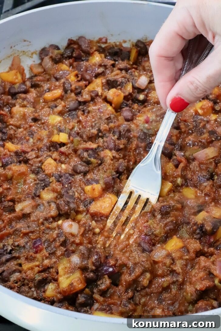 Vegetarian Cheesy Bean and Rice Burrito Recipe 7 bean burrito filling in a skillet with a fork smashing the beans