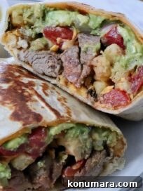 california burrito filled with carne asada and french fries cut in half and stacked up on a plate with a bowl of green salsa in the background