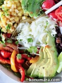 Zesty Chipotle Salad with Avocado, Corn and Lime 7 salad in a bowl topped with fajita veggies, avocado, corn, cheese, beans and tomatoes, with a fork in the middle of the bowl