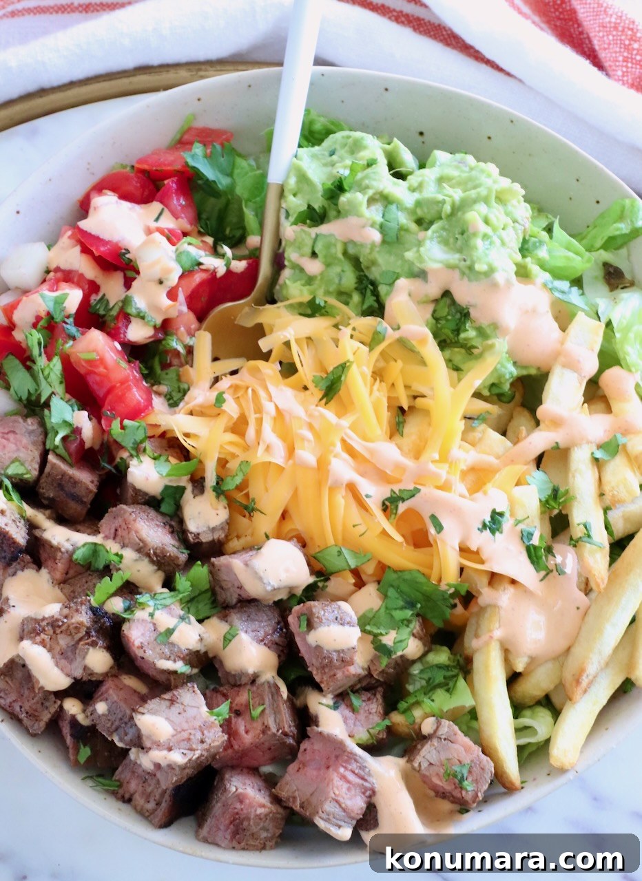 bowl filled with diced carne asada, shredded cheese, guacamole, and pico de gallo with a fork in the middle