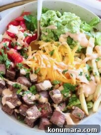 bowl filled with diced carne asada, french fries, cheese, pico de gallo and guacamole, with a fork in the middle