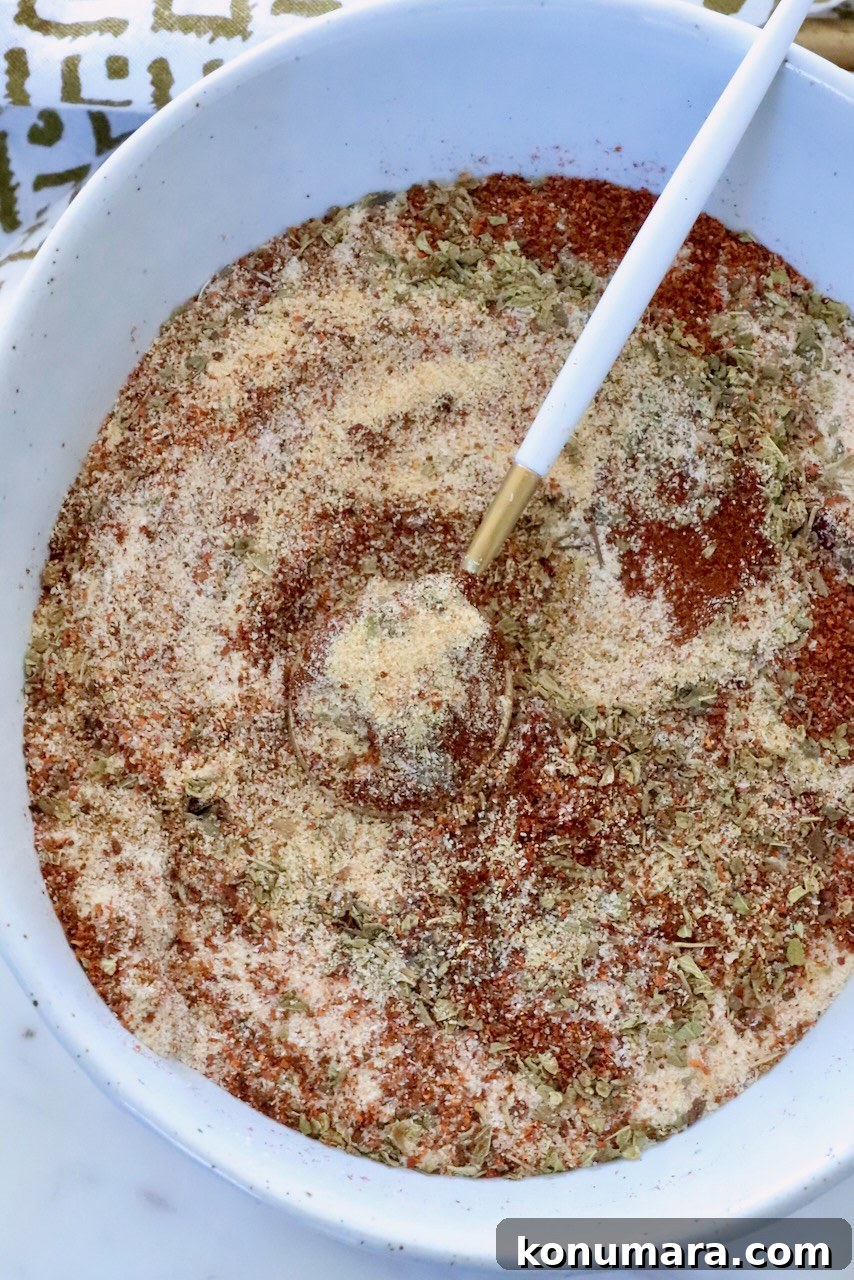 dried herbs and spices mixed together in a white bowl with a small spoon