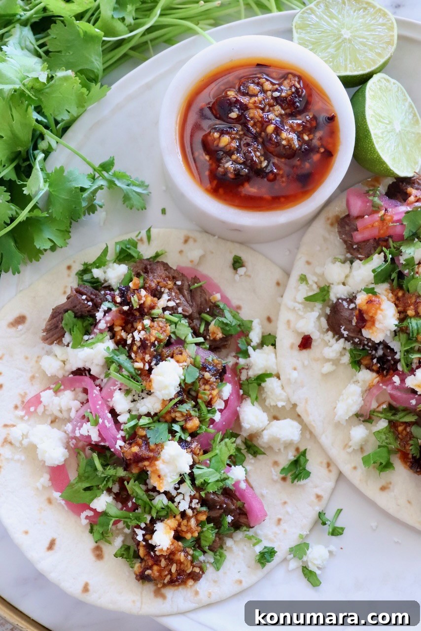 shredded beef barbacoa tacos on a plate topped with salsa macha, pickled onions, and cilantro