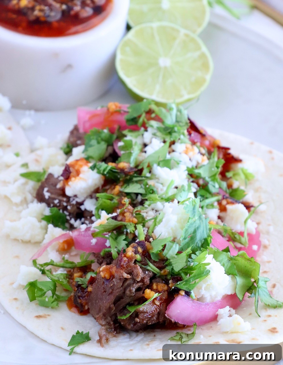 beef barbacoa taco on a plate with salsa macha, limes, cilantro, and pickled onions