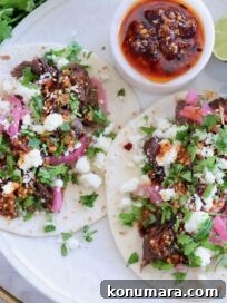 two tacos on a plate topped with beef barbacoa, crumbled cheese, pickled onions, salsa macha, and cilantro