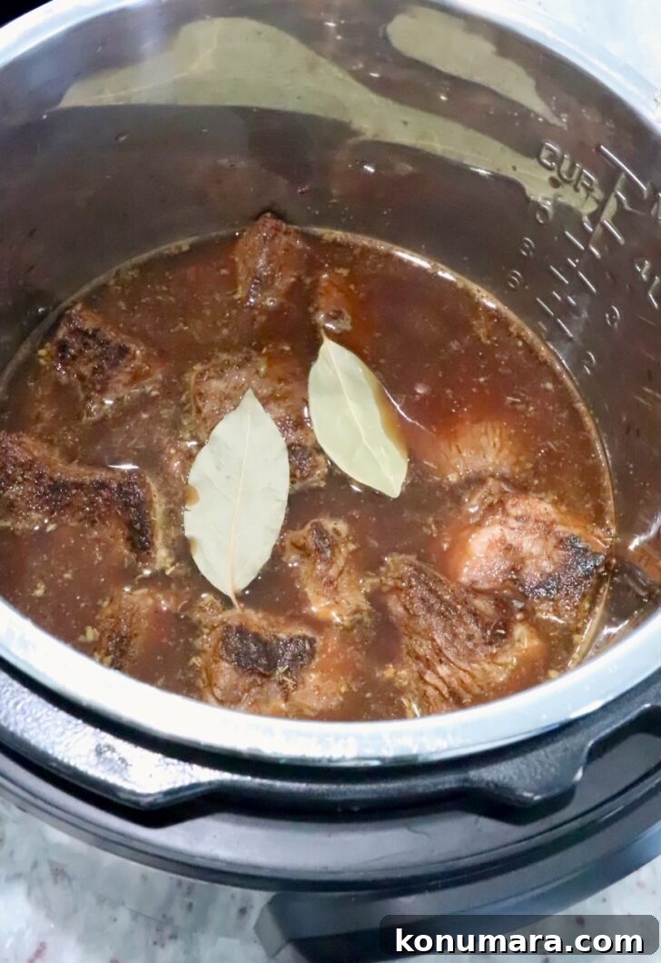 pieces of beef, covered with beef broth and bay leaves in an Instant Pot