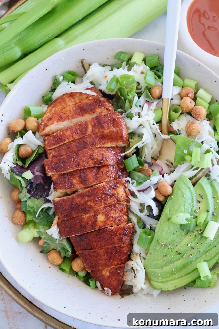 sliced buffalo chicken breast on top of a salad in a bowl with sliced avocado and a fork