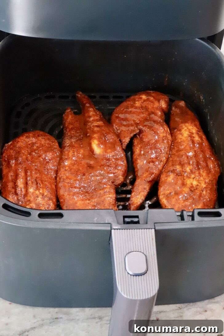 cooked chicken breasts brushed with buffalo sauce in an air fryer basket