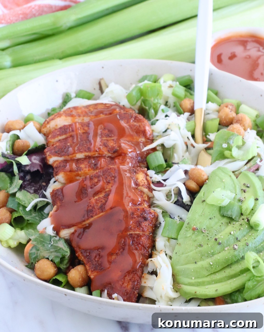 sliced chicken topped with buffalo sauce on top of a salad in a bowl with sliced avocado